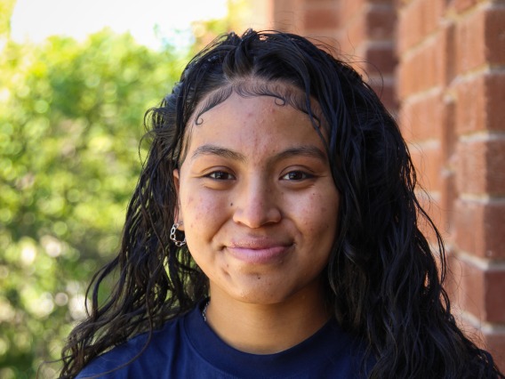 A headshot image of student staff Shanae Dosela with a brick building in the background