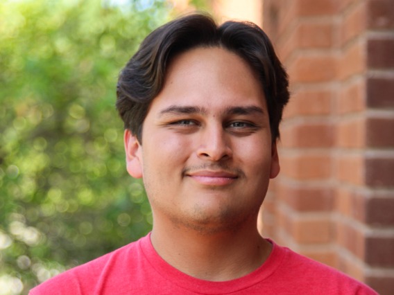 A headshot image of student staff Eric Trujillo with a brick building in the background