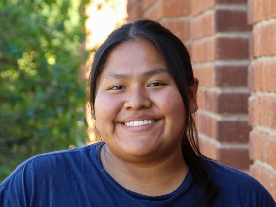 A headshot image of student staff Ariel Freddie with a brick building in the background