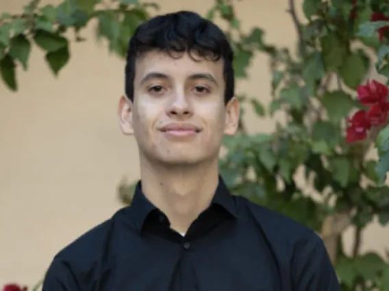 A headshot image of student staff Joshua with a rose bush in the background