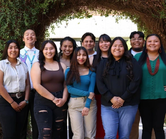 Group photo of Native American Student Affairs staff all standing in front of a grass covered building.