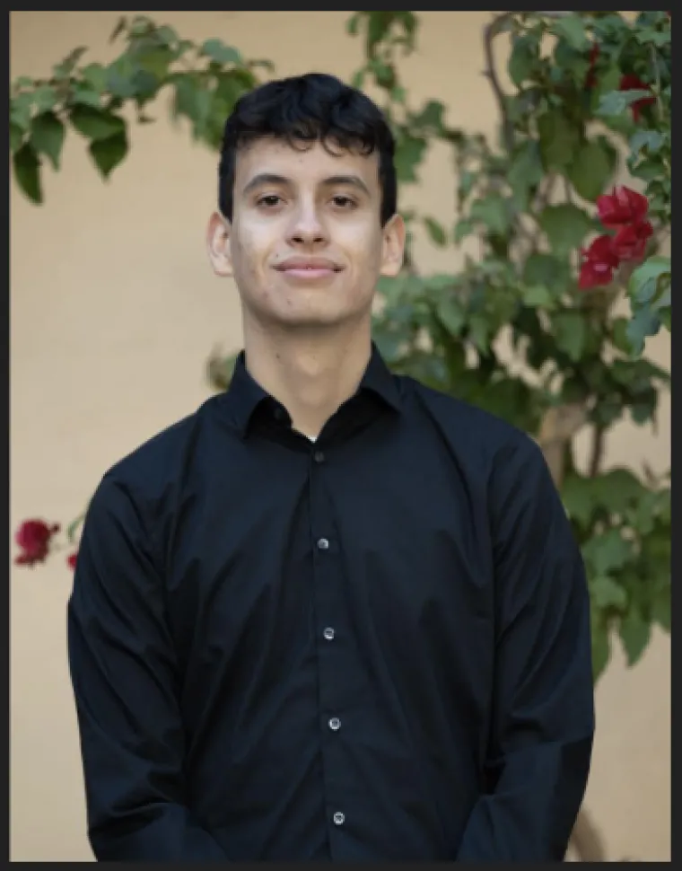 A headshot image of student staff Joshua with a rose bush in the background